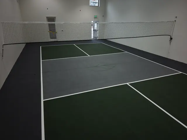 Indoor pickleball court with green playing areas, a gray center, black borders and a net.