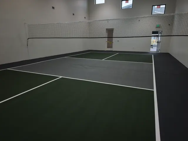 Indoor pickleball court with green playing areas, a gray center, black borders and a net.