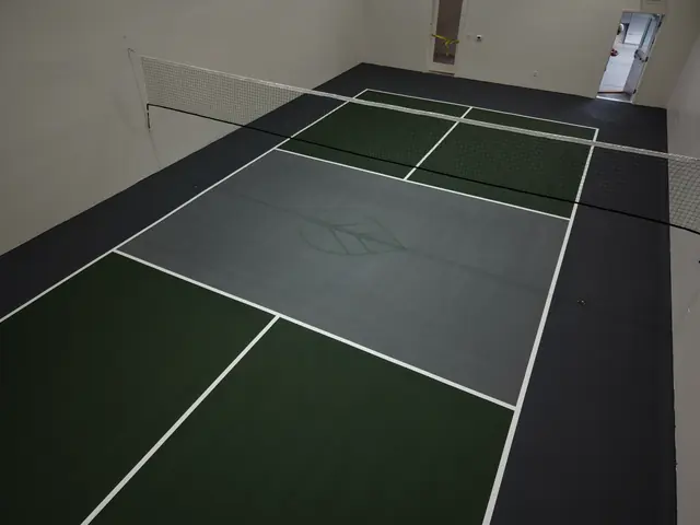 Indoor pickleball court with green playing areas, a gray center, black borders and a net.