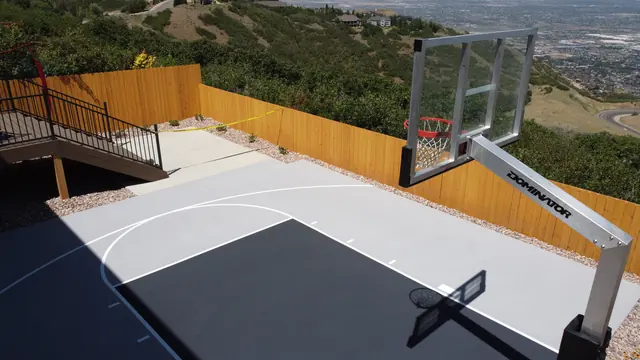 Gray backyard basketball half court with a dark key, white lines and wood perimeter fencing.