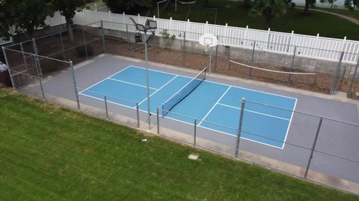 A fenced blue and gray backyard court with a net and basketball hoop.