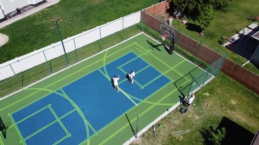 A blue and green shared court with a basketball hoop and center net.