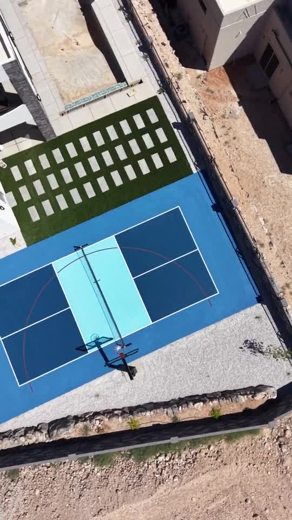 A blue court with a contrasting light blue key beside a modern home.