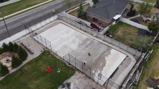 An aerial look at a concrete court base inside a fenced enclosure.