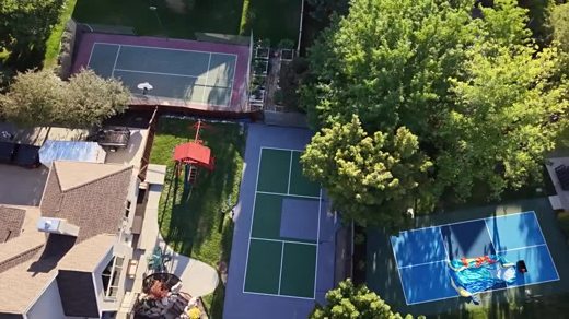 A green and gray backyard court framed by mature trees.