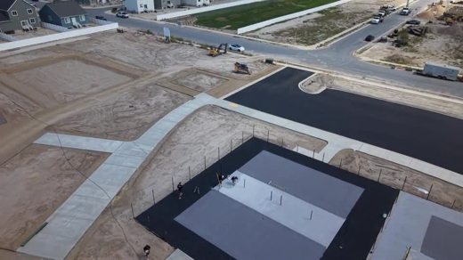An aerial view of two fenced court areas with contrasting gray surfaces.