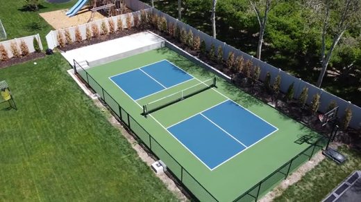 A blue pickleball court with green surrounds beside a lawn.