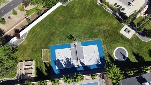 A light gray court with a blue border beside an open lawn.