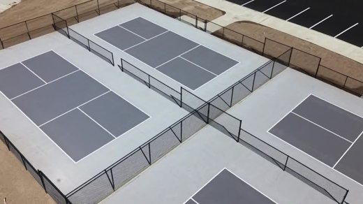 A close aerial view of four gray pickleball courts with black fencing.