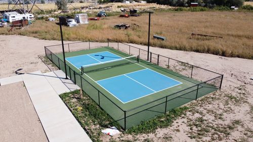 A fenced pickleball court with two blue playing areas and green border in a rural location.