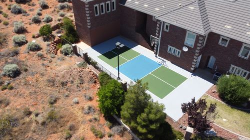 A backyard basketball court next to a brick house with a desert landscape on one side.