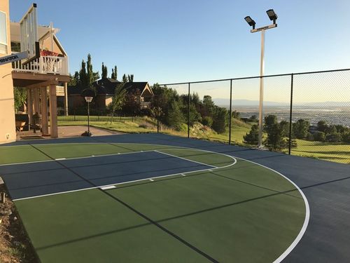 Outdoor basketball court with green and blue surface, two hoops, and a scenic hillside view.