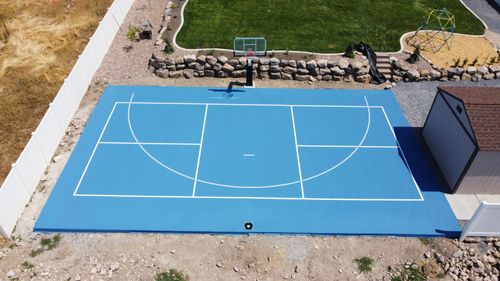 Backyard blue half-court basketball court with white lines, a hoop, and a small shed nearby.