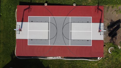 Aerial view of an outdoor basketball court with red, gray, and white markings and two hoops.