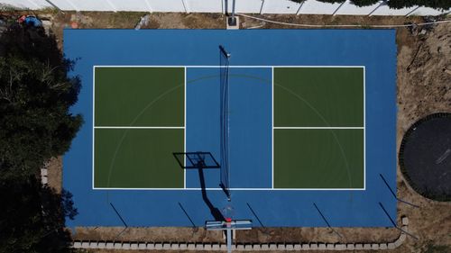 Aerial view of a blue and green outdoor sports court with a basketball hoop and volleyball net.