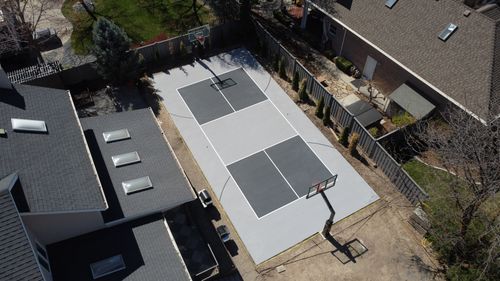 Aerial view of a private backyard with a newly painted half basketball court beside a house.