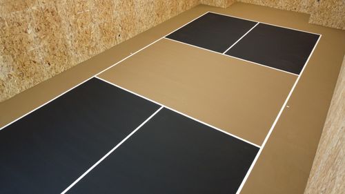 Indoor pickleball court with black and tan floor panels and wood-paneled walls.