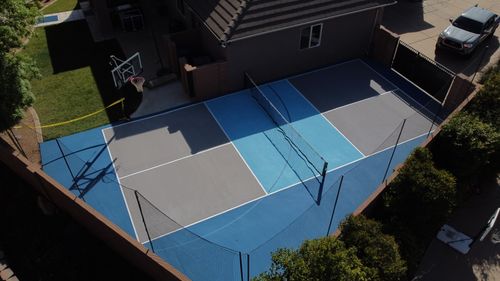 Backyard sports court with a basketball hoop and a net for tennis or pickleball next to a house.