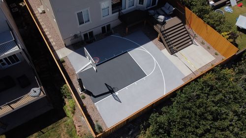 Aerial view of a small private basketball court with gray and white markings beside a house patio.
