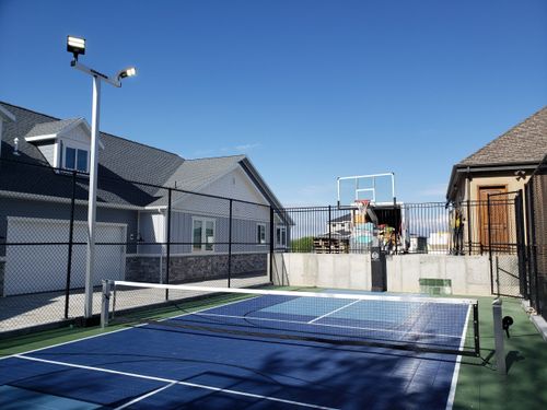 Outdoor sports court with a net for tennis or pickleball and a basketball hoop in a residential backyard.