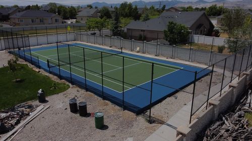 New outdoor tennis court with blue and green surface surrounded by black chain-link fence.
