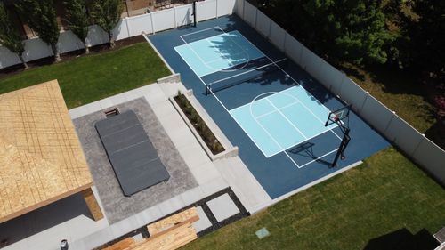 Aerial view of backyard with a blue basketball and pickleball court, patio, and lawn.