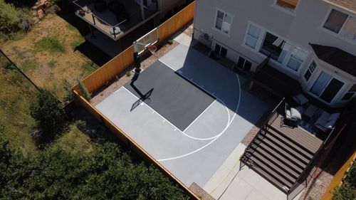 A backyard half basketball court next to a house with a fenced yard and outdoor seating.