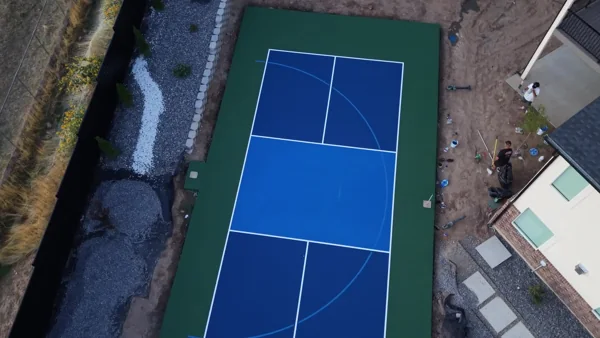 A closer aerial orbit shows the blue playing surface, green surround, and white court markings.