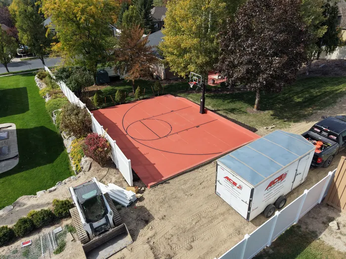 Aerial view of a red backyard basketball half court with black game lines and a single hoop