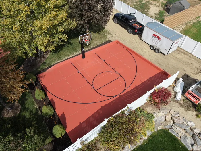 Wide aerial view of the red basketball half court and surrounding backyard