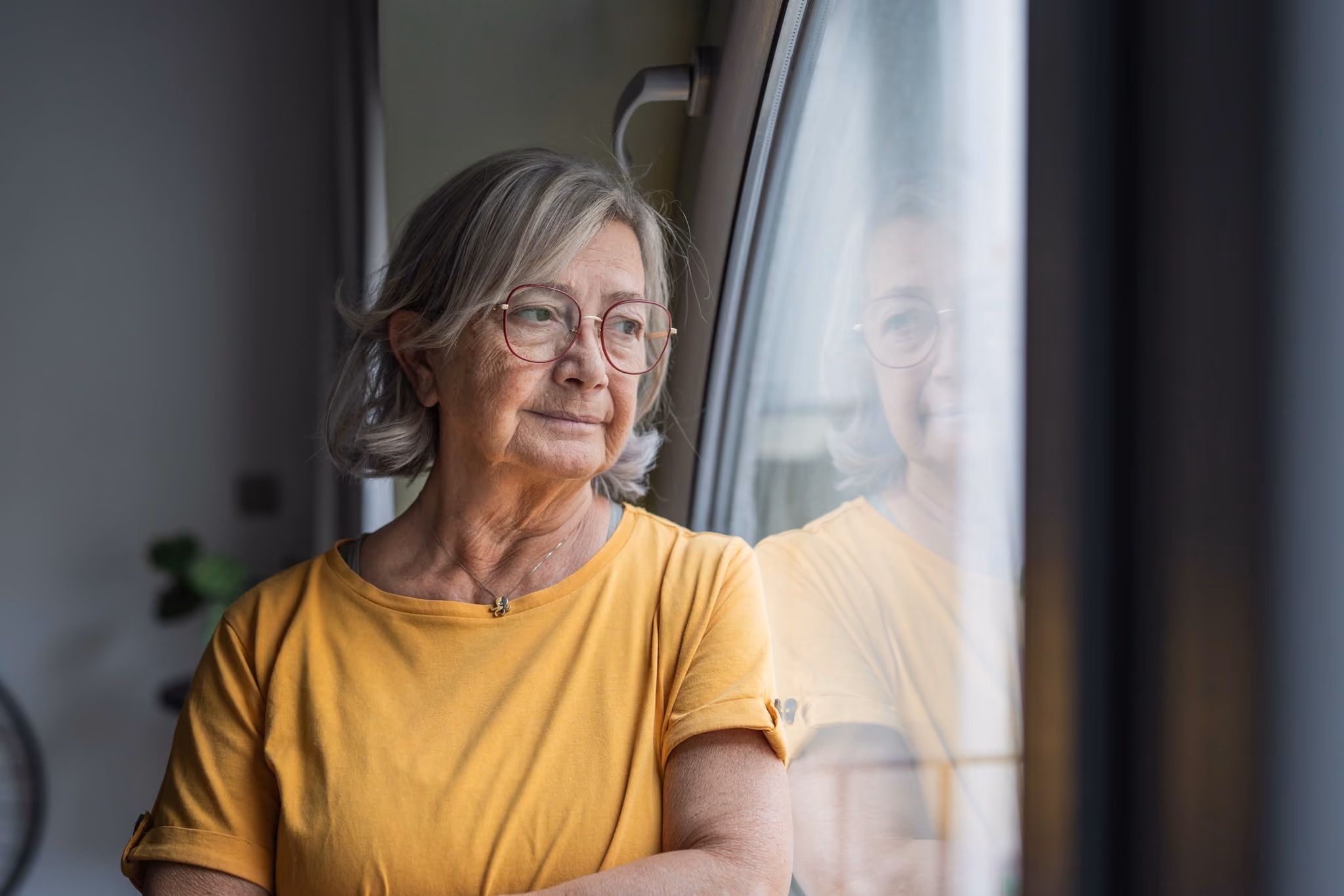 Senior woman standing and looking out of a window
