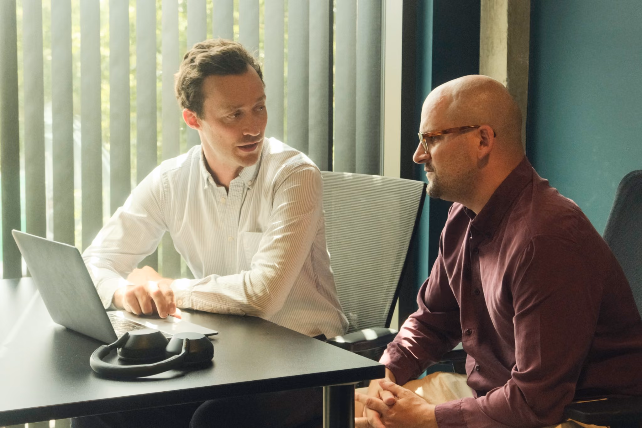 Two colleagues talking across a desk with a laptop in an office
