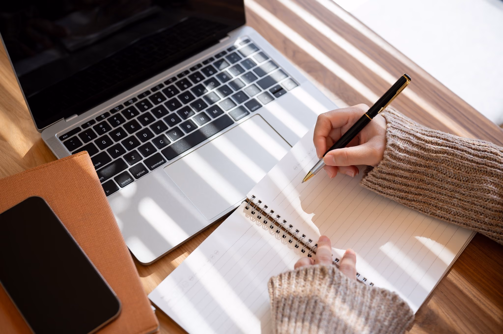 Person taking notes in a notebook beside a laptop