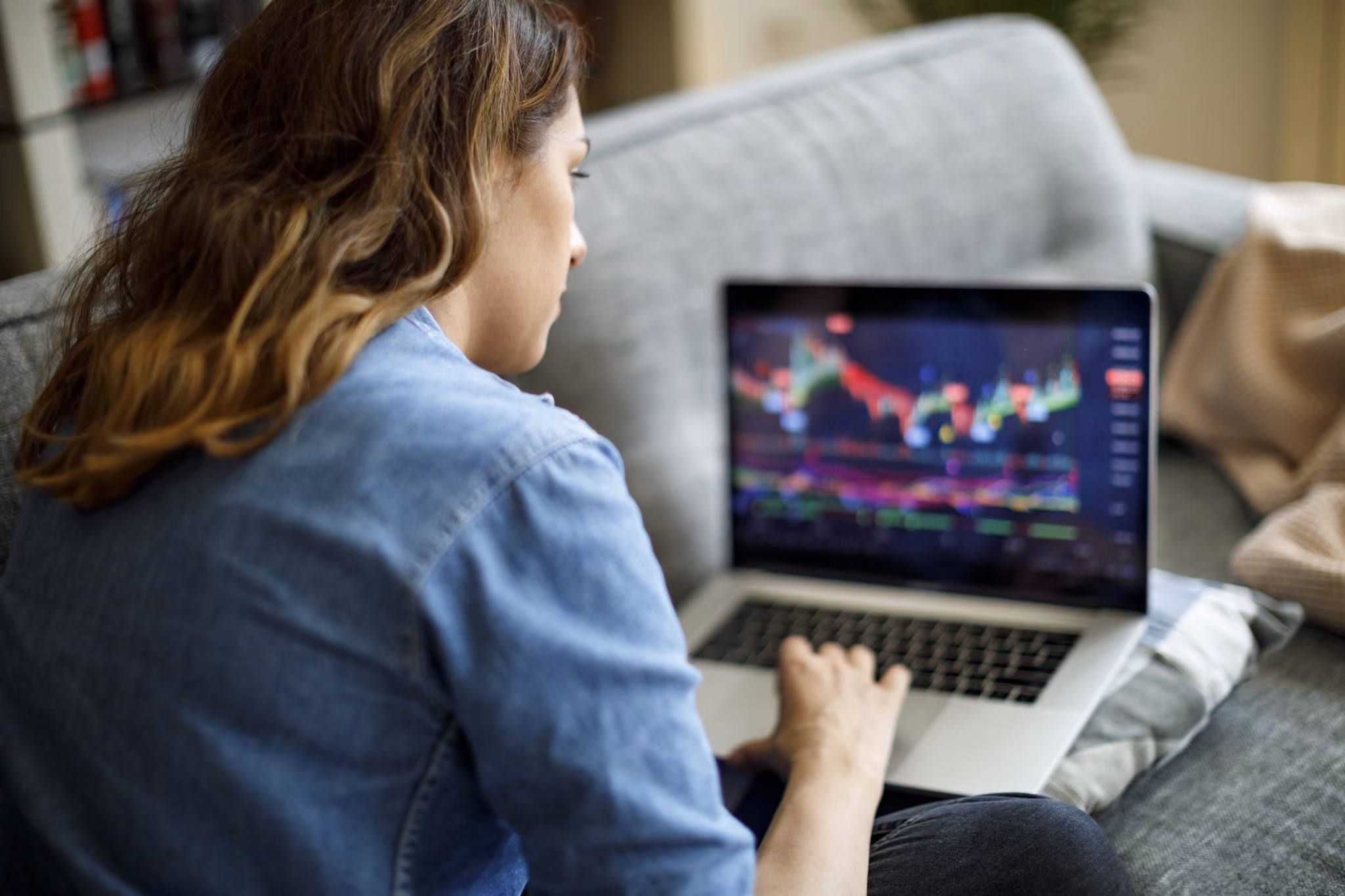 Woman looking at trading charts on a laptop on the sofa