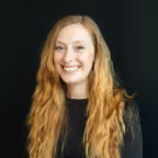 Smiling woman with long wavy blonde hair wearing a black top against a black background.
