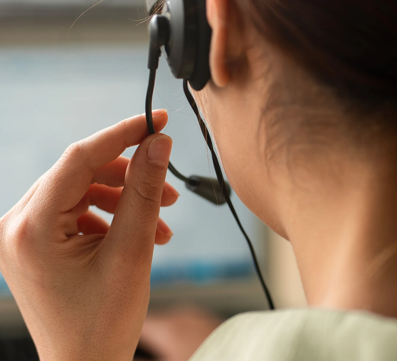 Close-up of a person adjusting a black headset microphone near their ear, with a blurred background.