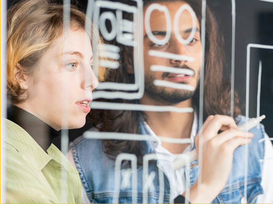 Two people collaborate and discuss ideas while drawing wireframe sketches on clear glass.