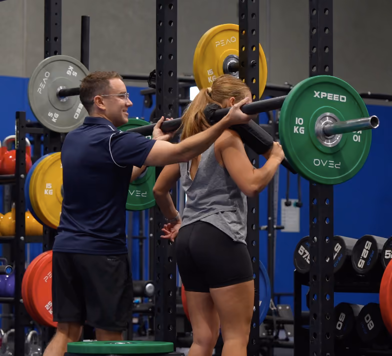 helping client do squats at peaq gym