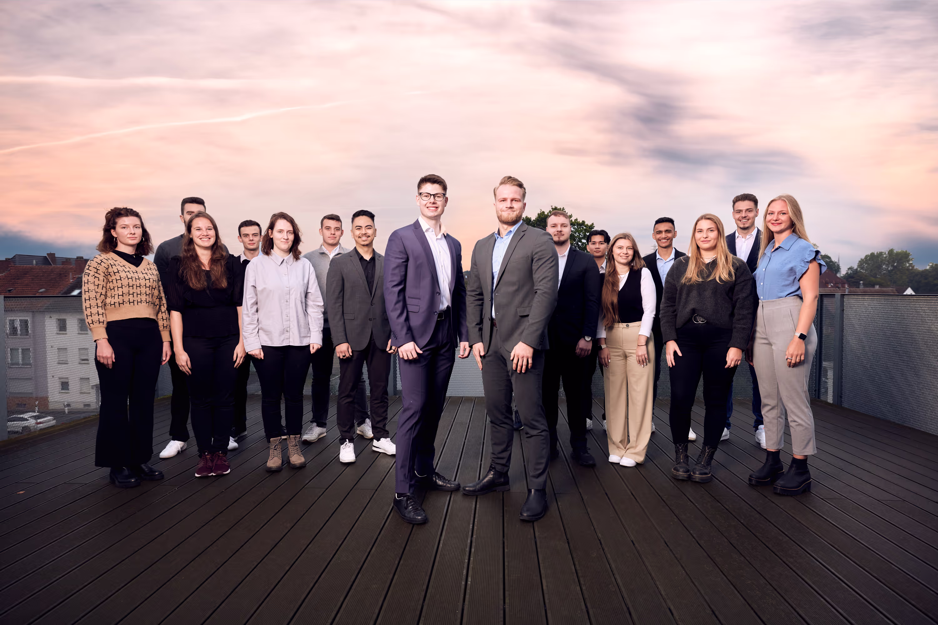 Das Team von PG Digital steht gemeinsam auf einer Dachterrasse bei Sonnenuntergang und blickt freundlich in die Kamera.