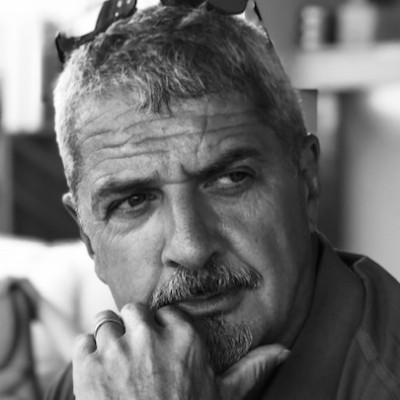 Black-and-white portrait of a man with short gray hair resting his chin on his hand, wearing sunglasses on his head.