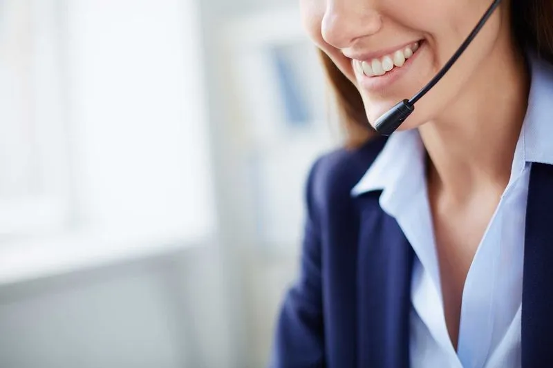 A woman wearing a headset smiles as she speaks, likely during a customer service call.