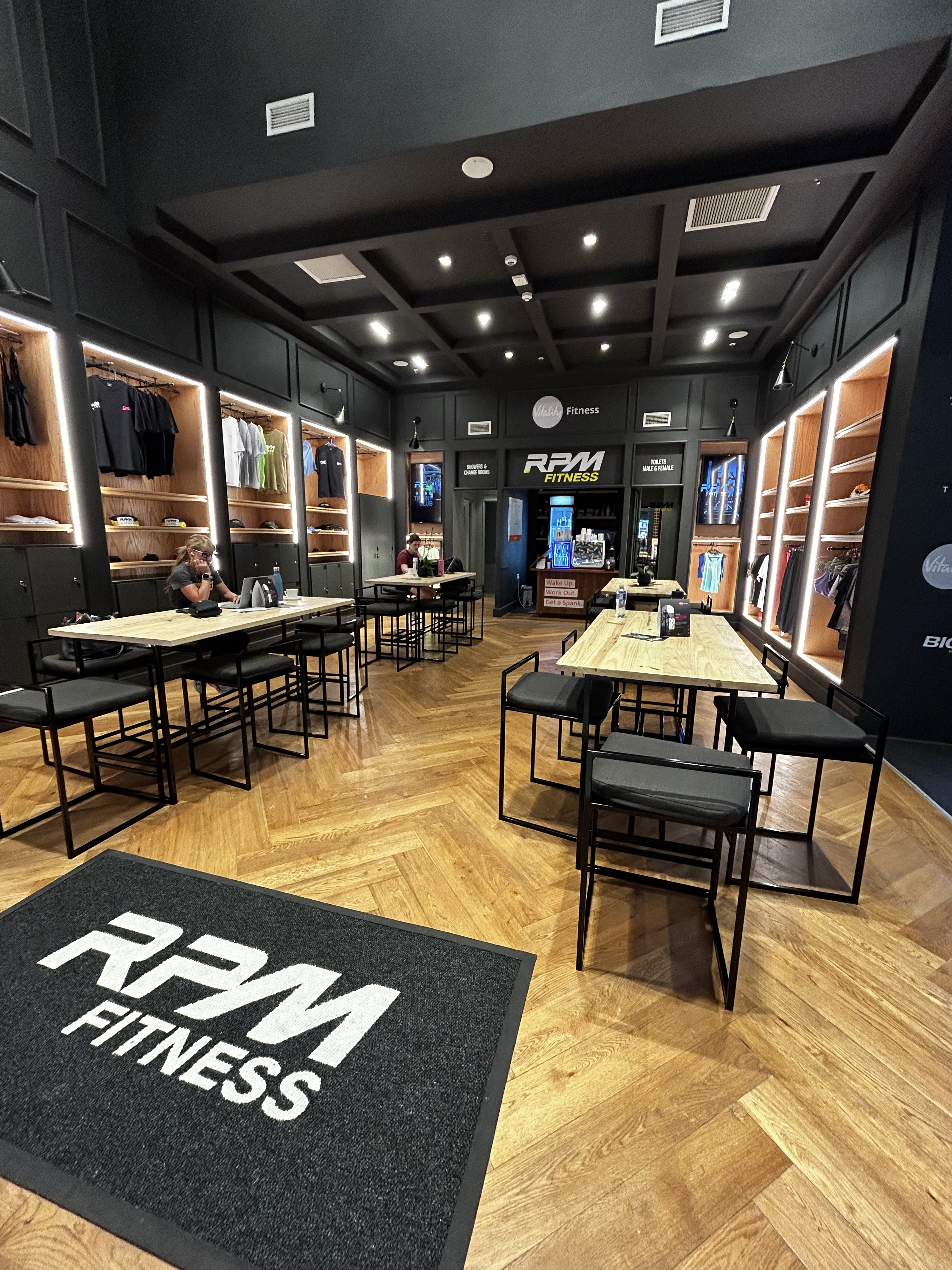 Modern gym interior with rows of exercise bikes, treadmills, and illuminated honeycomb ceiling lights.