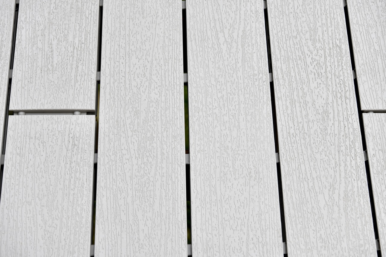 Close-up of beige wood decking with water and wooden post in the background.