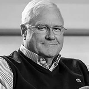 Portrait of an older man with glasses wearing a sweater vest over a striped shirt.