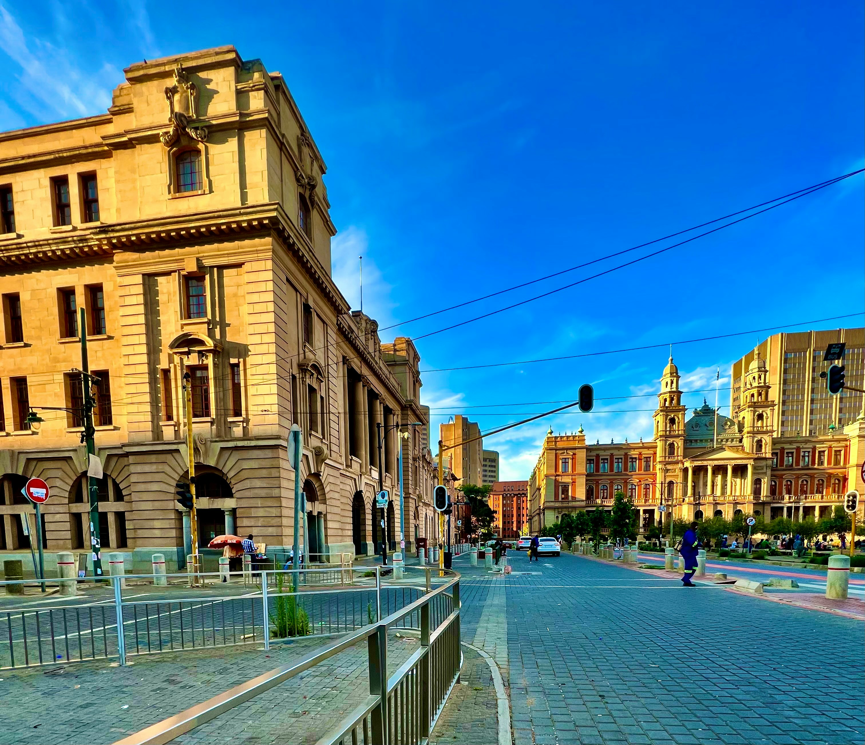 City street with historic buildings and pedestrians under a clear blue sky in late afternoon light.