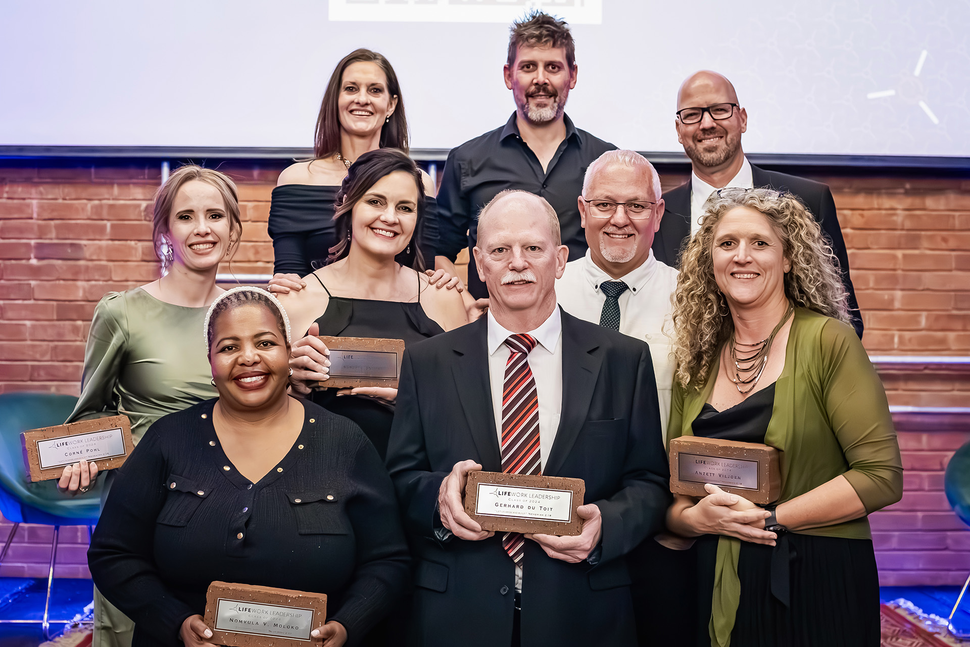 Nine people dressed formally smiling and holding leadership awards in a group photo.