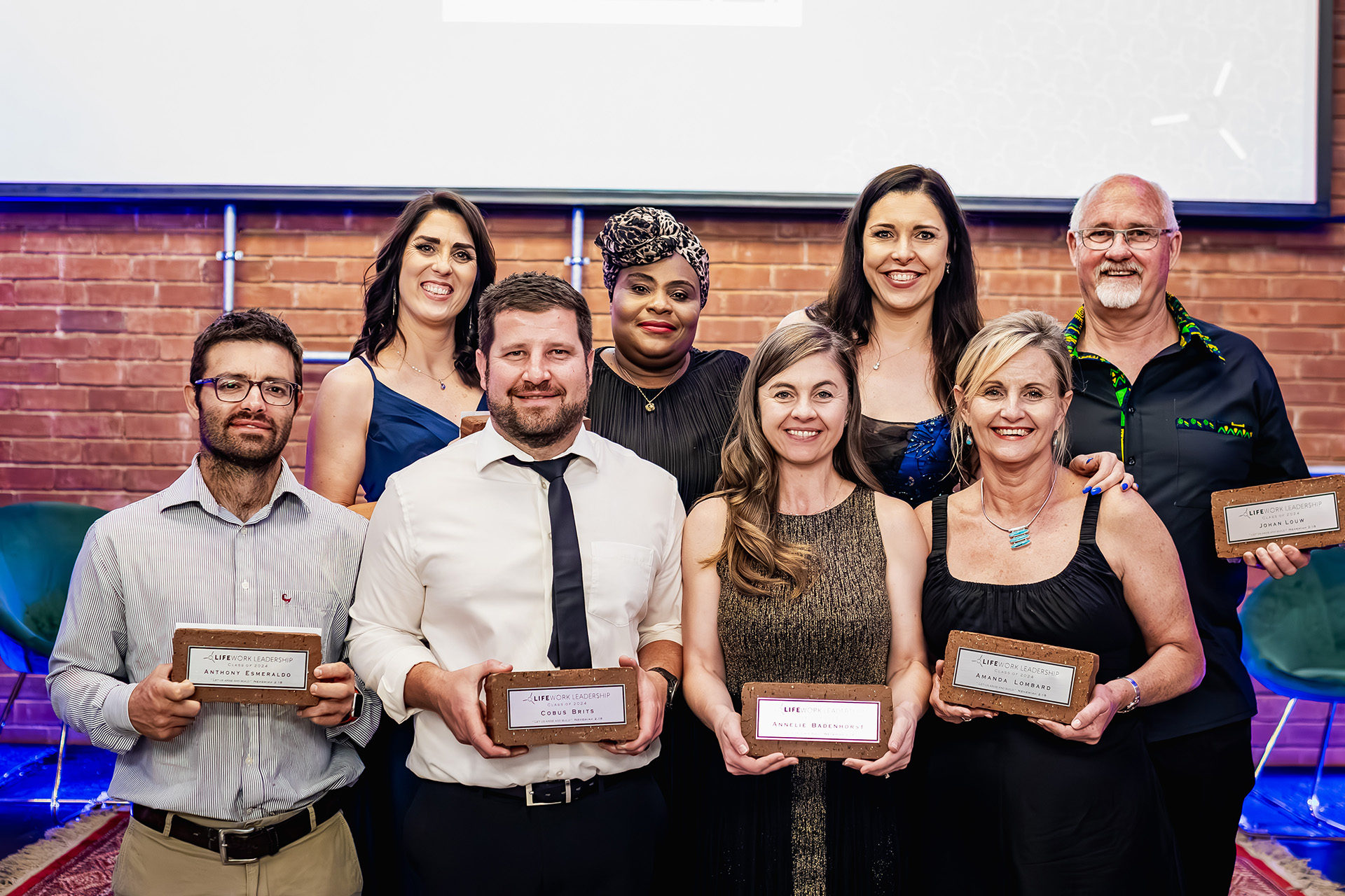 Seven people smiling and holding LifeWork Leadership award plaques in front of a brick wall.