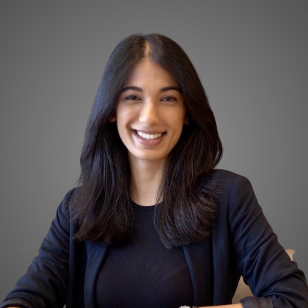 Smiling woman with long dark hair wearing a black blazer and top against a gray background.
