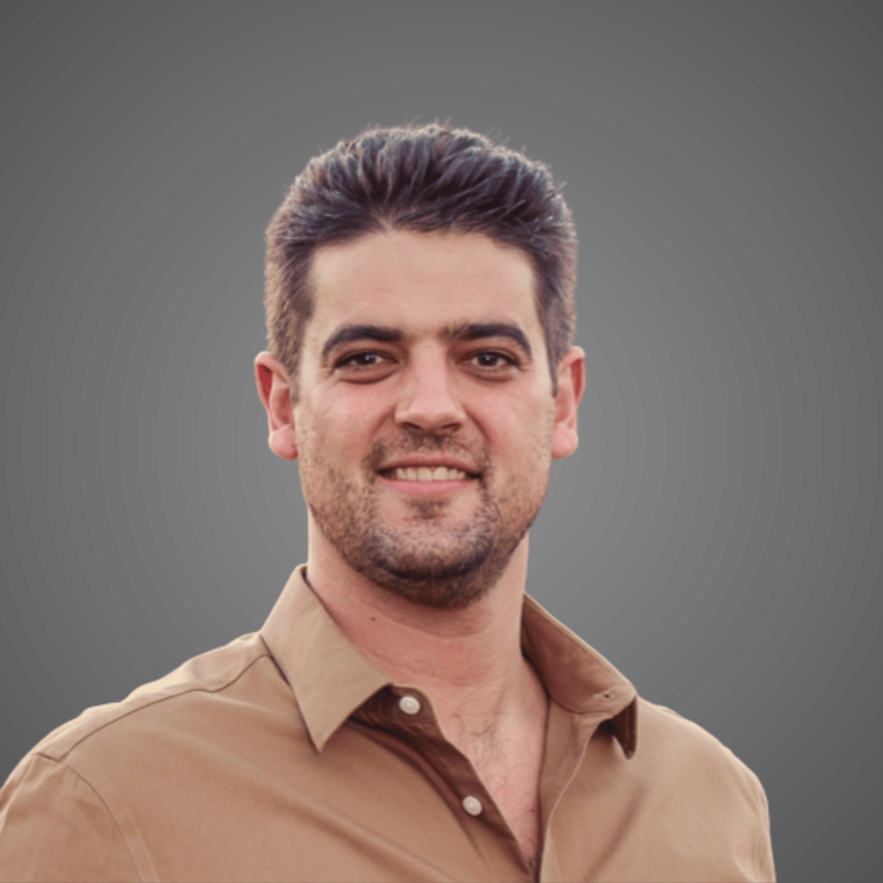 Smiling man with short dark hair and light beard, wearing a light brown button-up shirt.