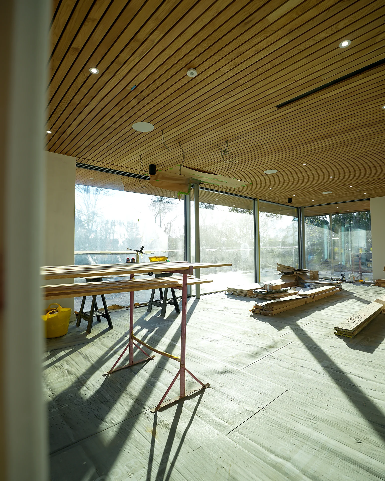 Inside a new glazed extension during fit-out, with a timber-lined ceiling